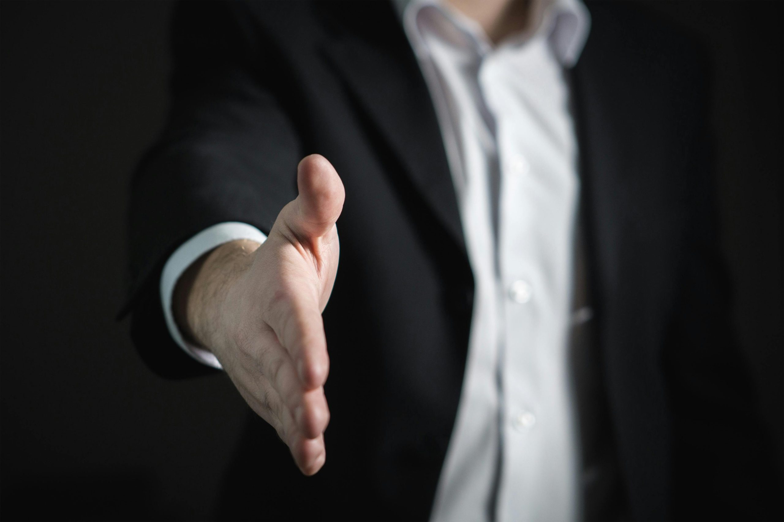 A person in a suit extends their hand to offer a handshake